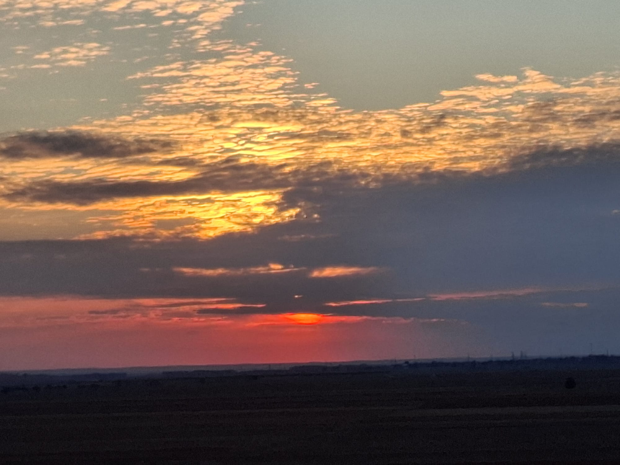 Apus roșiatic printre nori peste câmpie